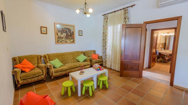 A living room with two sofas, a coffee table, and two green stools. There is a door leading to a bathroom with a sink and mirror.