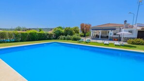 A rectangular swimming pool with a clear blue water surface, surrounded by a well-maintained lawn and a white fence.