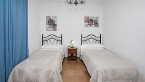 Une chambre avec deux lits simples, une table de chevet avec une lampe et deux tableaux abstraits accrochés aux murs.