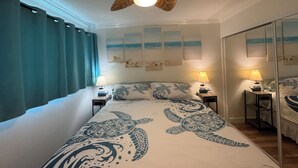 Une chambre à coucher avec un lit, deux tables de chevet avec des lampes, un ventilateur de plafond et un grand miroir.