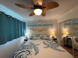Une chambre à coucher comprenant un lit, deux tables de chevet, un ventilateur de plafond et un grand miroir.