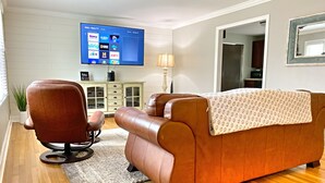A living room with a brown leather sofa, a brown leather chair, a flat-screen TV mounted on the wall, a wooden cabinet, and a lamp. - Quiet home in the Kernersville near Winston Salem, Greensboro, High Point (Kernersville)
