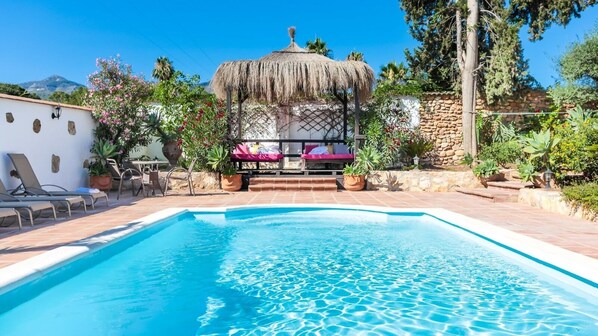Relax by the serene pool surrounded by a lush garden and a shaded gazebo.