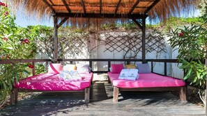 Relax in a serene outdoor space with two comfortable beds under a shaded pergola surrounded by lush greenery.