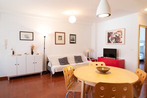 Una sala de estar moderna con un sofá blanco, un aparador rojo, un televisor y una mesa de comedor con sillas.