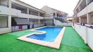 A swimming pool with a blue center, surrounded by a green deck and white buildings with balconies. - Global Vacacional: Apartment with pool in Corinto beach (Sagunto)