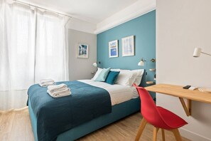A bedroom with a bed, a desk, a chair, and a window with curtains.
