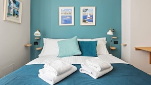 Een hotelkamer met een bed, twee wandlampen, een wand in teal en twee ingekaderde afbeeldingen.