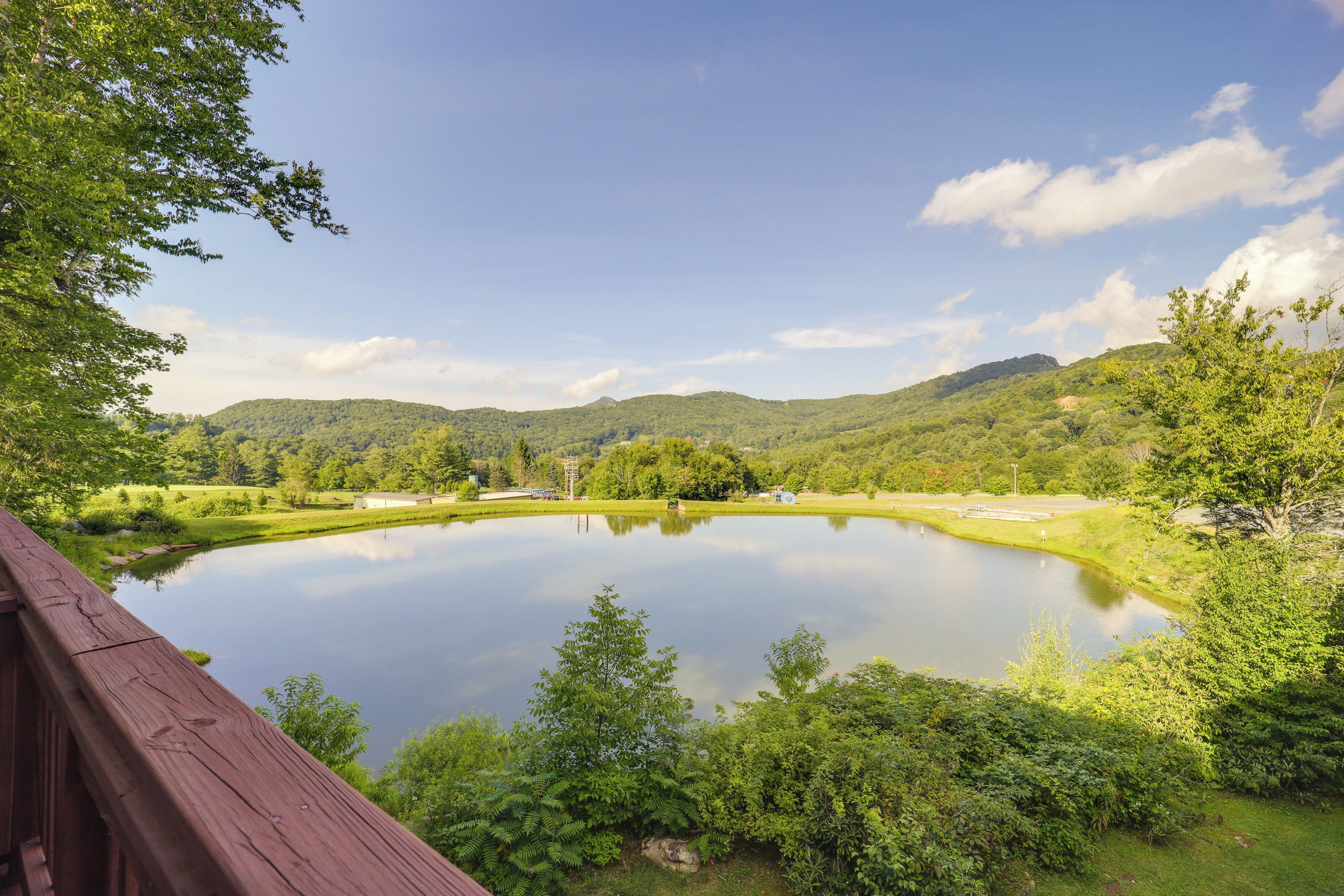 A serene lake surrounded by lush greenery and hills, viewed from a wooden deck.