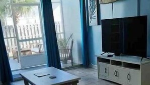 Una sala de estar con televisor, una mesa de madera y un ventanal corredero que da al exterior.