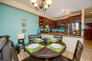 A dining area with a round table set for four, surrounded by wooden chairs. A chandelier hangs above the table, and the walls are painted teal.