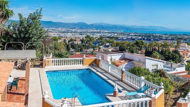 Ein Pool auf dem Dach mit Blick auf eine Stadtlandschaft und Berge im Hintergrund.