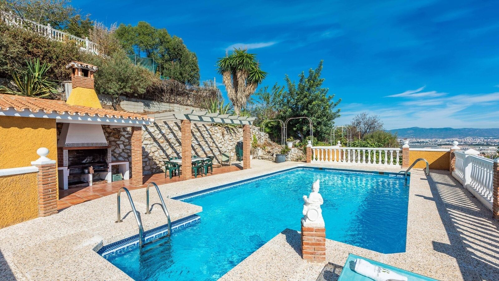 Una piscina en la azotea con un muro de piedra, zona de barbacoa y vistas a la ciudad.