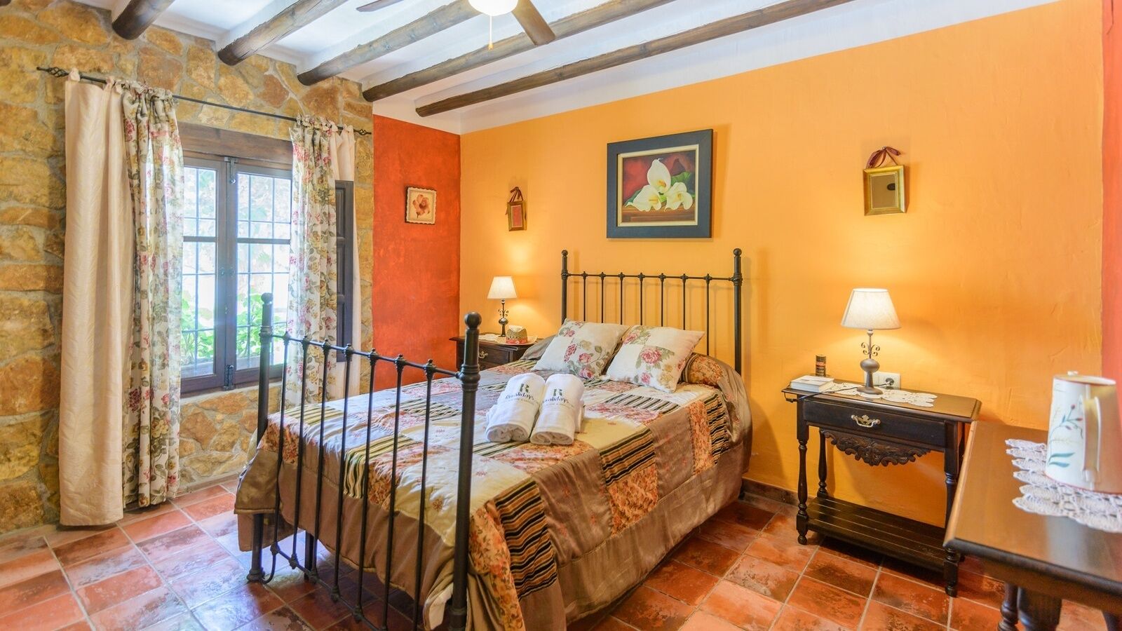Una camera da letto con un letto, due comodini, una finestra con tende e una parete in pietra.