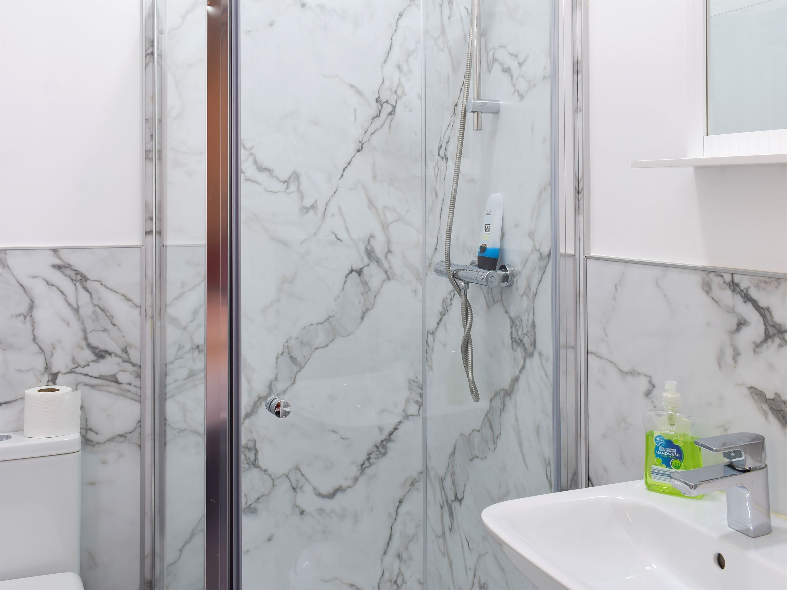 Ein Badezimmer mit einer gläsernen Duschkabine, einem weißen Waschbecken und einer Marmorwand.