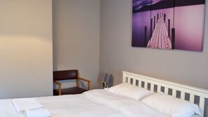 Quarto de hotel com cama, almofadas, uma cadeira, um abajur e uma pintura na parede.