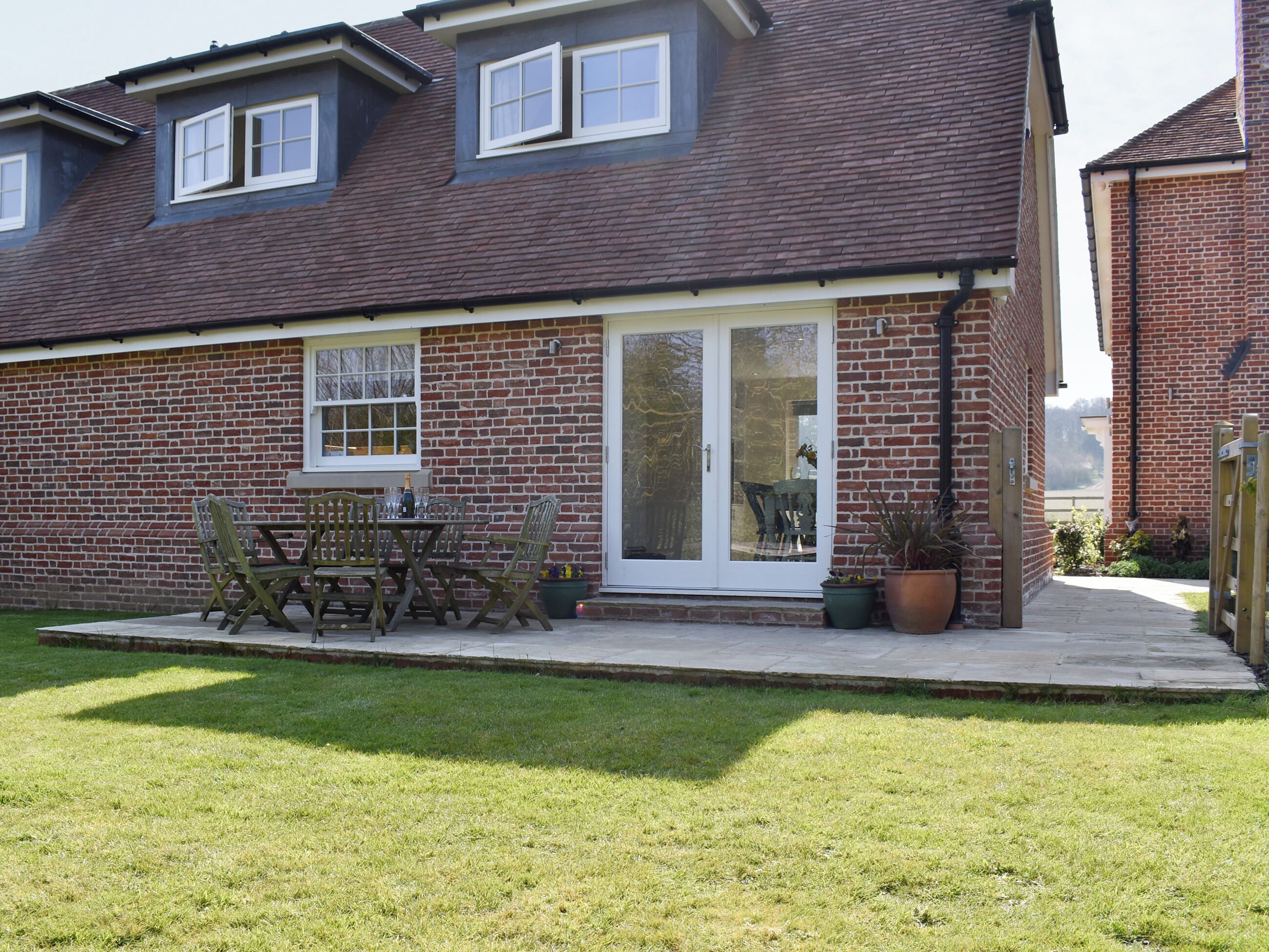 A two-story brick house with a patio and a dining table with chairs.