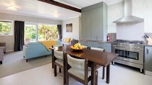 A modern kitchen with a dining area, featuring a wooden table, chairs, a stove, and cabinets. - Cliffscapes Punakaiki (Punakaiki)