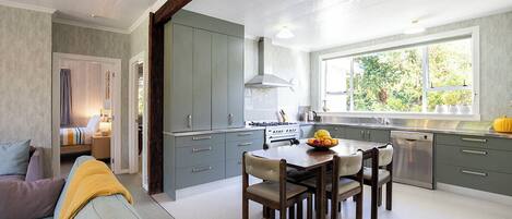 A modern kitchen with grey cabinets, a dining table with chairs, and a window with a view of greenery.