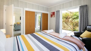A hotel room with a bed, a seating area with a chair, a wardrobe, and a view of greenery outside. - Cliffscapes Punakaiki (Punakaiki)
