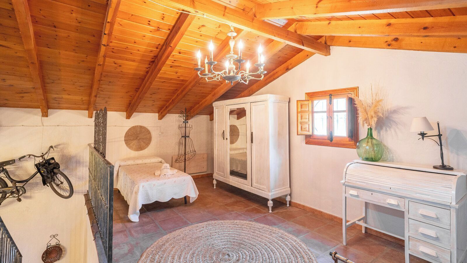 A bedroom with a bed, a wardrobe, a desk, a bicycle, and a chandelier.