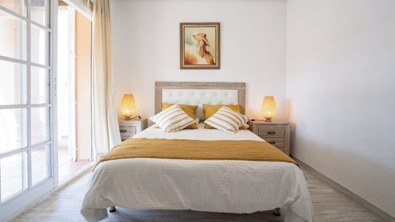 Een slaapkamer met een bed, twee nachtkastjes, een raam en een schilderij aan de muur.