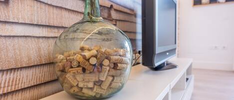 A glass bottle filled with wine corks on a white surface with a television in the background.