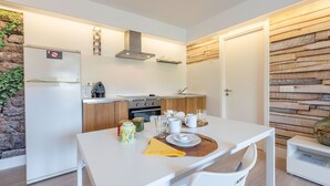A compact kitchen with a white countertop, a stove, and a sink. There is a dining table with a yellow placemat and a vase on the side. - Casa Ami Guaro by Ruralidays (Málaga)