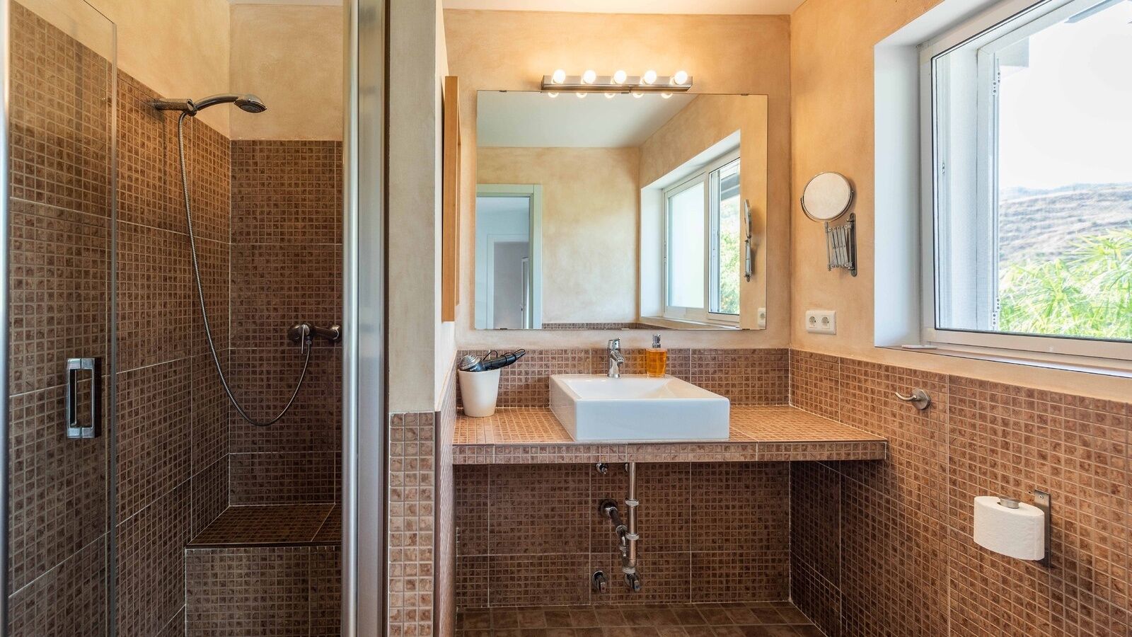 A bathroom with a shower, a sink, a mirror, and a window.