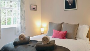 Een net opgemaakt bed met opgerolde handdoeken, een bedlamp en een ingelijste foto aan de muur.