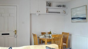 Een eethoek met een tafel gedekt voor twee personen, een witte deur en een plank met decoratieve objecten.