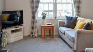 Een woonkamer met een televisie, een bank, een klein houten tafeltje en een raam met gordijnen.