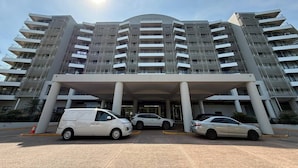 A multi-story hotel with a modern architectural design, featuring a central entrance with a covered walkway and several vehicles parked in front. - Rustic Sunset Horizon: Oceanview ~ Balcony Dining (Darwin City)