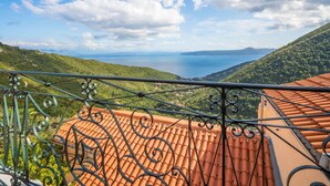 Un balcón con vistas a un paisaje costero, tejas de terracota y barandilla de metal.