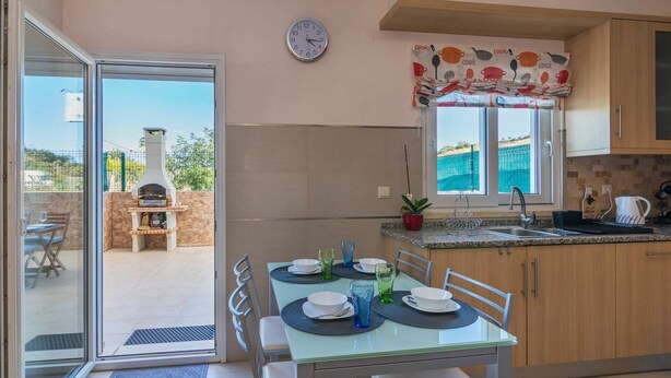 A modern kitchen with a dining area, a clock on the wall, and a view of the outdoors.