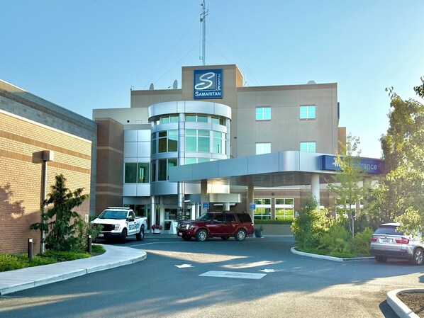 A modern hospital building with a Samaritans sign, a security vehicle, and a BMW parked in front.