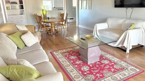 Ein Wohnzimmer mit einer Couch, einem Couchtisch, einem Fernseher und einem Essbereich mit Stühlen und Tisch.