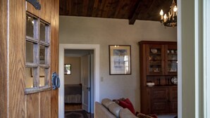 A wooden door with glass panels, a living room with a sofa and a cabinet, and a hallway leading to another room. - Emmie's | Great Location (Fredericksburg)