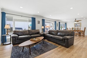 Ein modernes Wohnzimmer mit zwei Ledersofas, einem Couchtisch und einem Essbereich mit Holztischen und -stühlen.