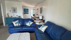 Una sala de estar con un sofá seccional azul, una mesa de centro de madera y un ventilador de techo.