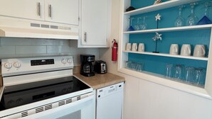 Una cocina con armarios blancos, una estufa negra, una cafetera y un lavavajillas.