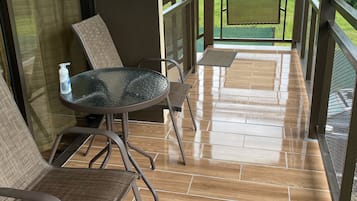 Un balcón cubierto con una mesa y sillas, vista a un paisaje verde y suelo de baldosas.