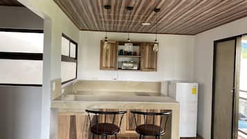 Una cocina con techo de madera, dos taburetes de bar, horno empotrado y refrigerador.