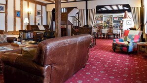 A cozy living room with exposed wooden beams, a piano, a bookshelf, and a red patterned carpet. - 4 bedroom accommodation in Pulham Market, near Diss (Pulham Market, near Diss)