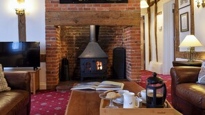 A cozy living room with a brick fireplace, a television, leather sofas, and a coffee table with books and a mug. - 4 bedroom accommodation in Pulham Market, near Diss (Pulham Market, near Diss)
