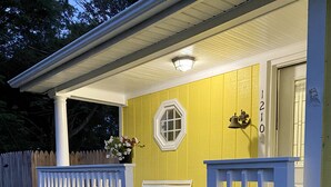 A porch with a white bench, a white picket fence, and a yellow wall with the number 1210. - Sunny Place Cottage,  Your Pet-Friendly Home away from Home! 🐾 (Colonial Beach)