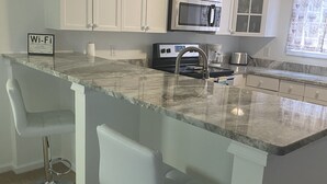 A kitchen with white cabinets, a granite countertop, a stainless steel sink, and a microwave. - Sunny Place Cottage,  Your Pet-Friendly Home away from Home! 🐾 (Colonial Beach)