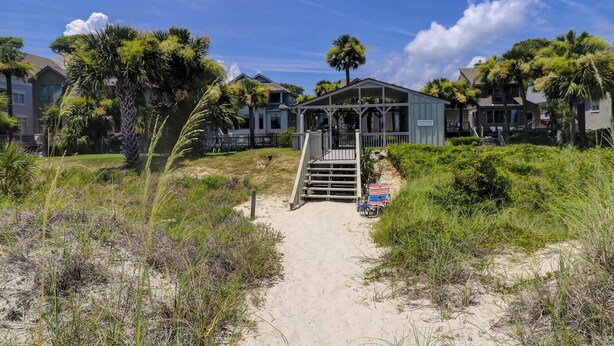 Una casa sulla spiaggia con un portico coperto, un sentiero di sabbia che vi conduce e un cartello con la scritta "Oceanwood Beach House".