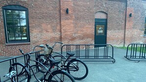 Um edifício de tijolos com uma porta e uma janela pretas. Bicicletas estão estacionadas na frente.