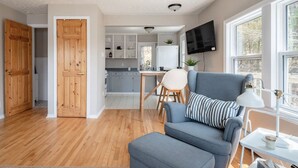 A modern living room with a blue sofa, a dining area with a wooden table, and a kitchen with white cabinets. - Private Lakefront Escape – Swim, Sip Wine & Stargaze – 25 Mins to Halifax (Brookside)